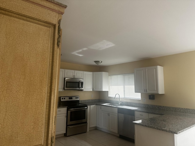 kitchen with light tile patterned floors, appliances with stainless steel finishes, a peninsula, white cabinetry, and a sink