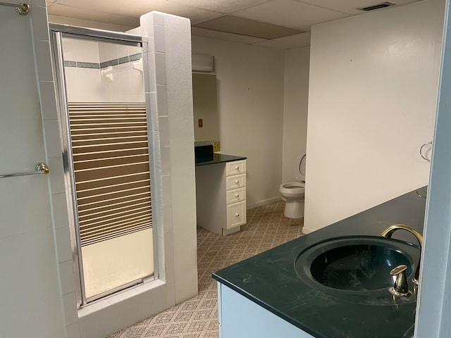 bathroom with vanity, toilet, a drop ceiling, and a shower with shower door