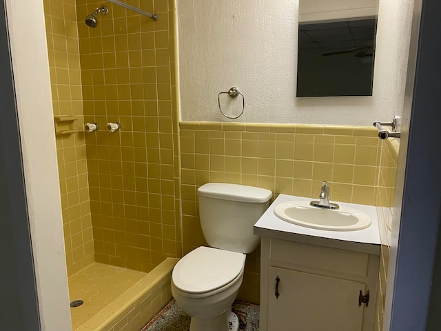 bathroom with a tile shower, vanity, toilet, and tile walls