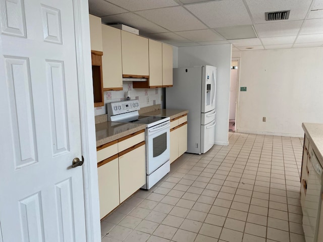 kitchen with a paneled ceiling, backsplash, white appliances, cream cabinets, and light tile patterned floors