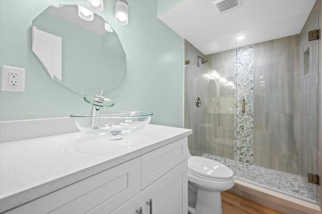 bathroom with hardwood / wood-style floors, toilet, a shower with door, and vanity