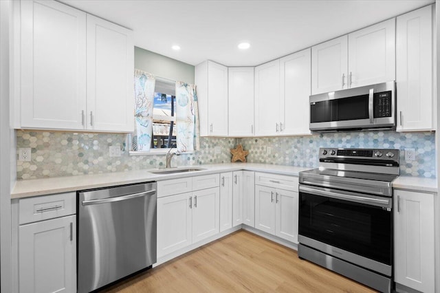 kitchen featuring stainless steel appliances, sink, decorative backsplash, white cabinetry, and light wood-type flooring