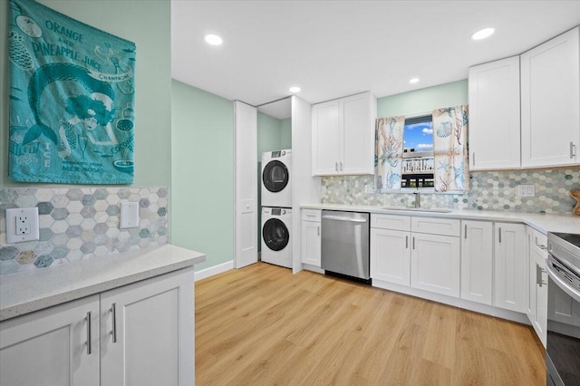 kitchen with light wood-type flooring, stainless steel appliances, stacked washer / dryer, sink, and white cabinets