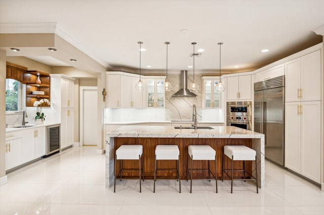 kitchen featuring a center island with sink, wall chimney range hood, sink, wine cooler, and stainless steel appliances