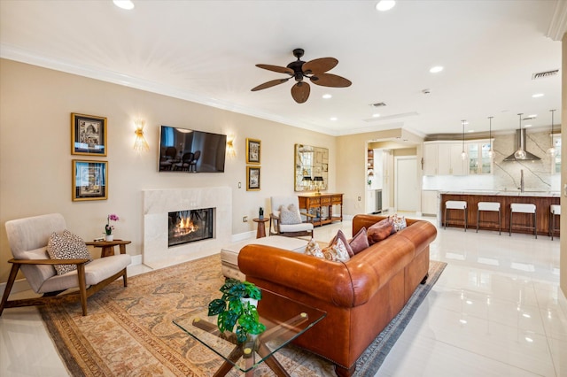 tiled living room featuring ceiling fan, sink, a premium fireplace, and crown molding