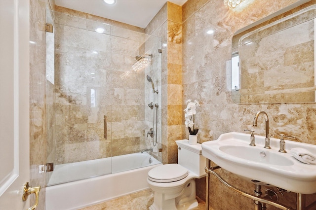 full bathroom with toilet, sink, bath / shower combo with glass door, and tile walls