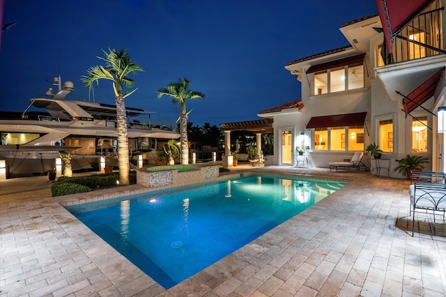 pool at night featuring an in ground hot tub and a patio