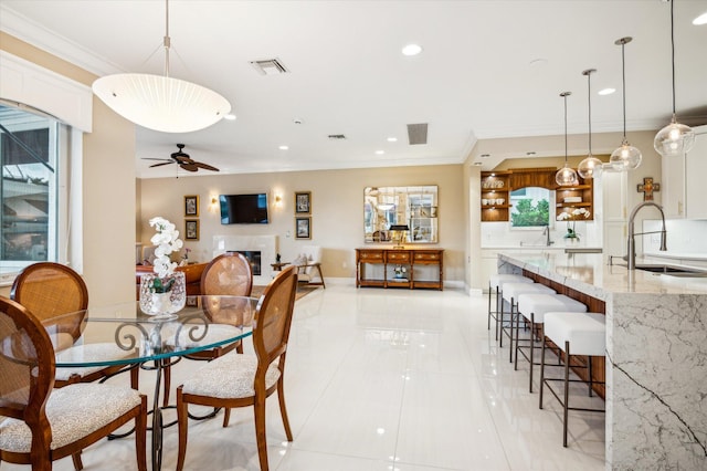 tiled dining space with ceiling fan, sink, and ornamental molding