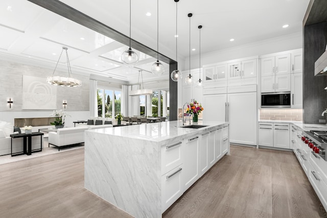 kitchen featuring black microwave, white cabinetry, a center island with sink, and pendant lighting