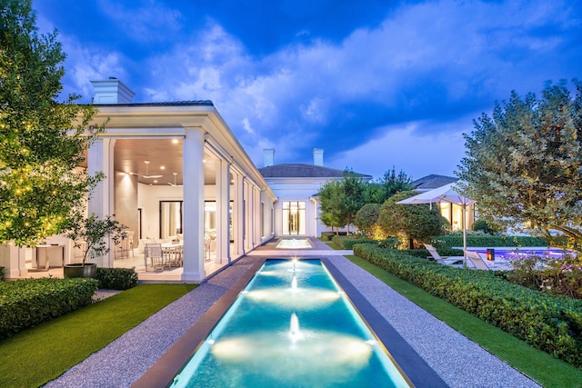 pool at dusk with pool water feature, a patio, ceiling fan, and french doors