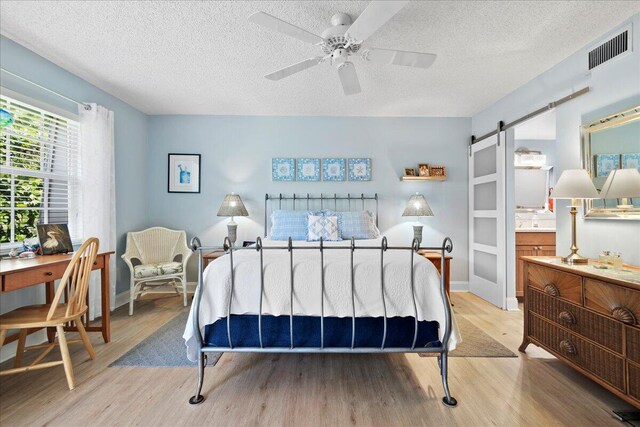 bedroom with a barn door, ceiling fan, a textured ceiling, and light hardwood / wood-style flooring