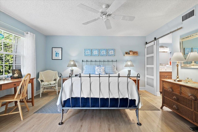 bedroom with visible vents, baseboards, a barn door, light wood-style floors, and a textured ceiling