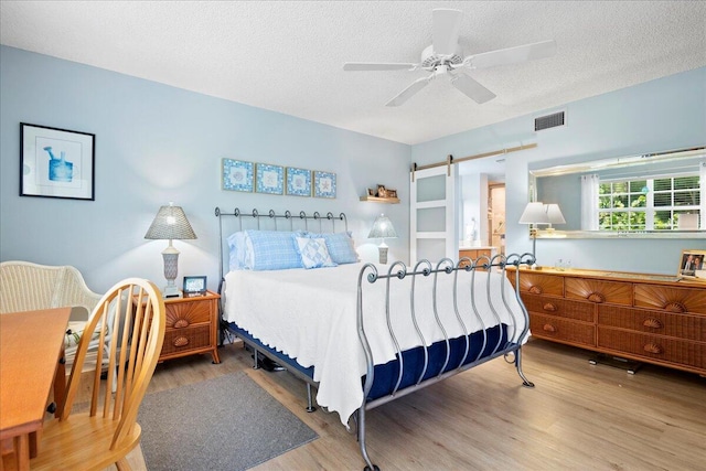 bedroom with a textured ceiling, a barn door, ceiling fan, and hardwood / wood-style flooring