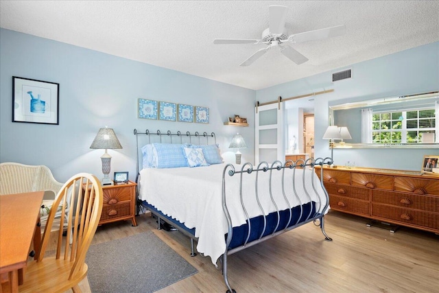 bedroom featuring ceiling fan, wood finished floors, visible vents, and a textured ceiling
