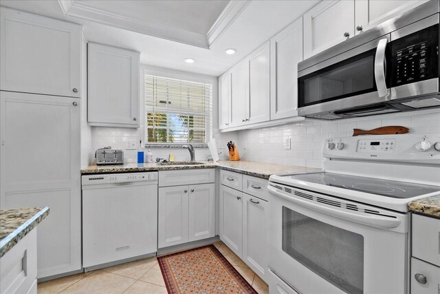 kitchen featuring white appliances, a tray ceiling, ornamental molding, decorative backsplash, and white cabinets