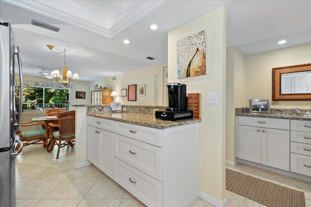 kitchen with light stone counters, light tile patterned floors, visible vents, freestanding refrigerator, and a notable chandelier