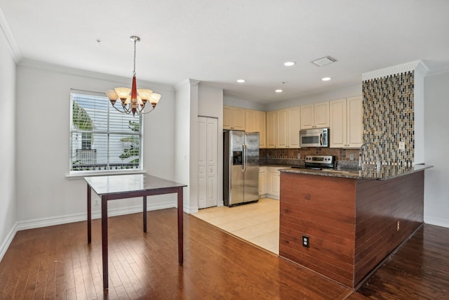 kitchen with appliances with stainless steel finishes, light wood-type flooring, ornamental molding, pendant lighting, and a chandelier