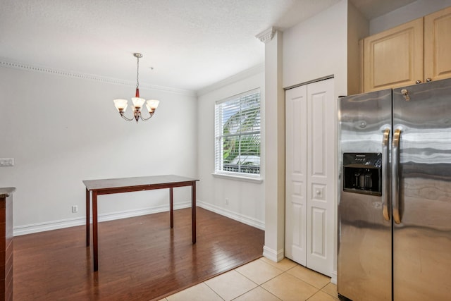 kitchen featuring hanging light fixtures, a notable chandelier, stainless steel fridge, light brown cabinetry, and light wood-type flooring