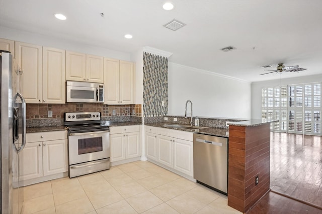 kitchen featuring kitchen peninsula, appliances with stainless steel finishes, backsplash, ceiling fan, and sink