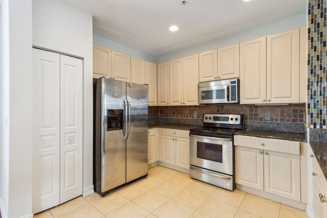 kitchen with light tile patterned floors, backsplash, stainless steel appliances, and dark stone counters