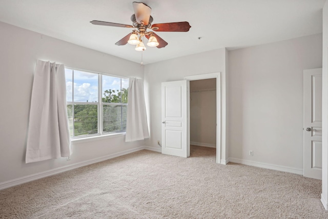 unfurnished bedroom with light carpet, a walk in closet, a closet, and ceiling fan