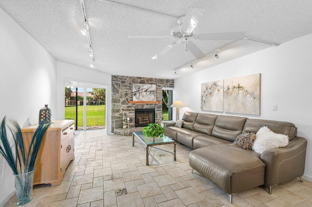 living room featuring track lighting, a fireplace, ceiling fan, and a textured ceiling