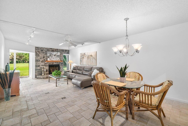 dining space featuring ceiling fan with notable chandelier, rail lighting, a textured ceiling, and a fireplace