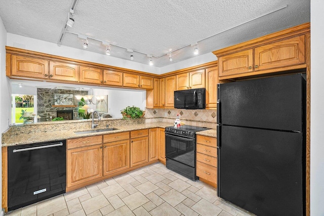 kitchen with sink, a fireplace, backsplash, light stone countertops, and black appliances