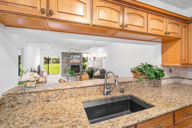 kitchen with light stone counters, track lighting, tasteful backsplash, a fireplace, and sink