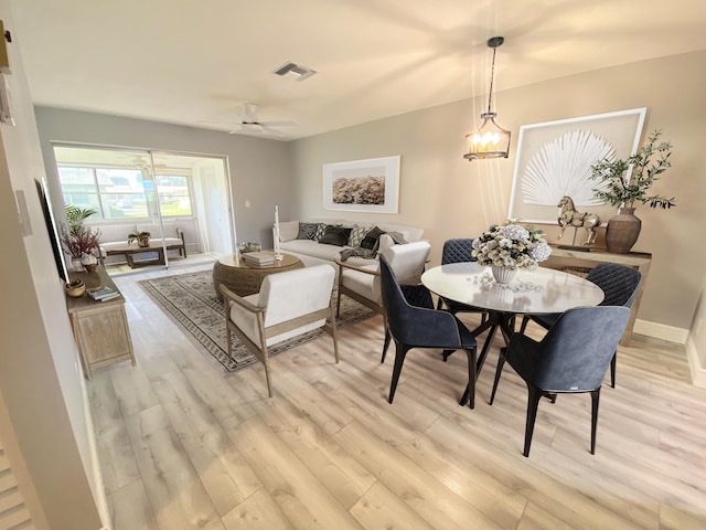 dining room with ceiling fan with notable chandelier and light wood-type flooring