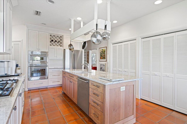 kitchen with white cabinetry, sink, a kitchen island with sink, light stone counters, and stainless steel appliances