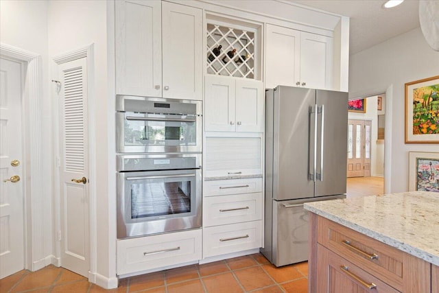 kitchen featuring light stone counters, stainless steel appliances, light tile patterned flooring, and white cabinets