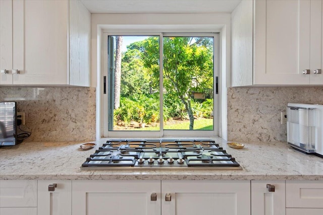 kitchen with stainless steel gas stovetop, white cabinets, and backsplash