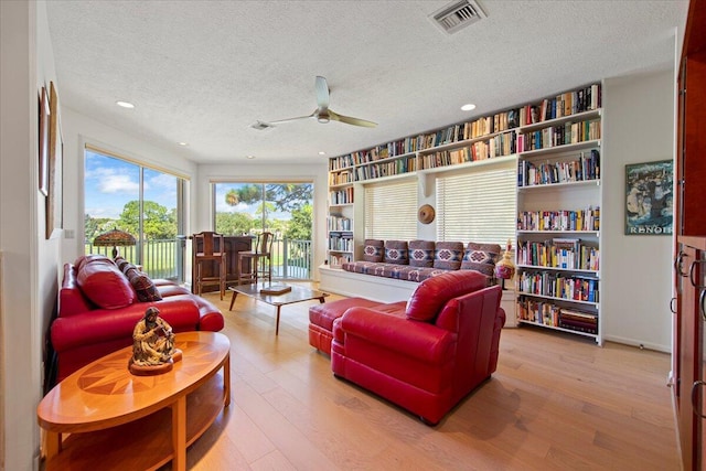 living room with ceiling fan, a textured ceiling, and light hardwood / wood-style flooring