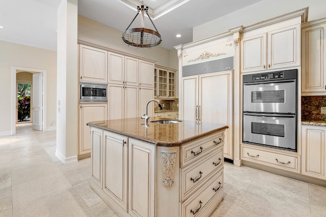 kitchen featuring sink, built in appliances, cream cabinets, pendant lighting, and a kitchen island with sink