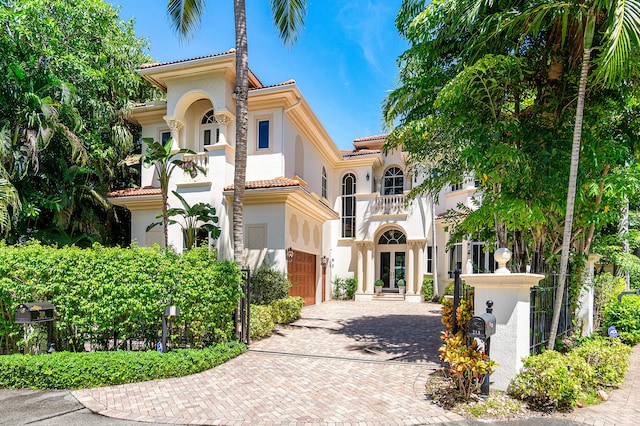 mediterranean / spanish house featuring a tile roof, stucco siding, decorative driveway, a garage, and a balcony