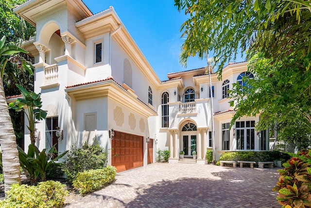 mediterranean / spanish-style house featuring a balcony, stucco siding, french doors, a garage, and decorative driveway