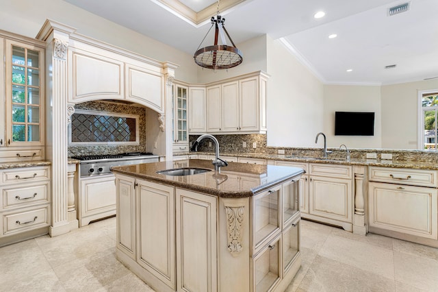 kitchen with a center island with sink, cream cabinets, sink, and tasteful backsplash