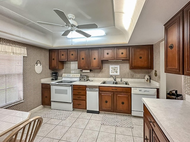 kitchen featuring a tray ceiling, light tile patterned flooring, sink, white appliances, and ceiling fan