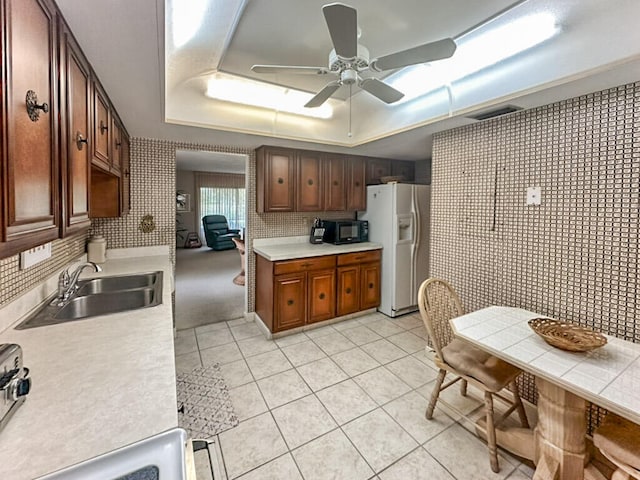 kitchen featuring light tile patterned floors, a tray ceiling, ceiling fan, white fridge with ice dispenser, and sink