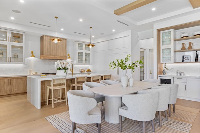 dining room featuring light wood-type flooring, beamed ceiling, and beverage cooler