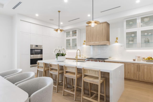 kitchen with pendant lighting, sink, white cabinetry, a kitchen island with sink, and stainless steel appliances