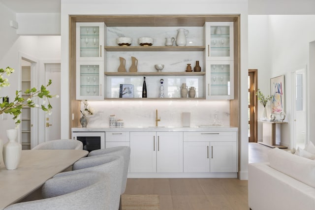 bar featuring white cabinets, wine cooler, decorative backsplash, sink, and light hardwood / wood-style flooring