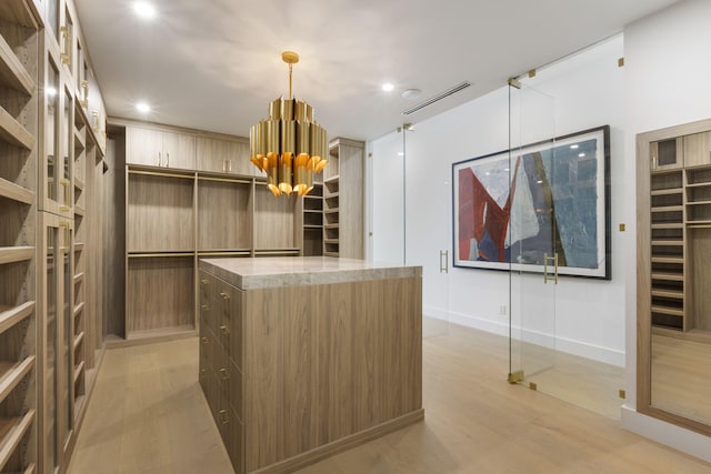 spacious closet featuring light hardwood / wood-style floors and an inviting chandelier