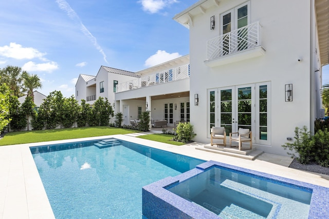 rear view of house featuring a patio area, french doors, a pool with hot tub, a balcony, and a yard