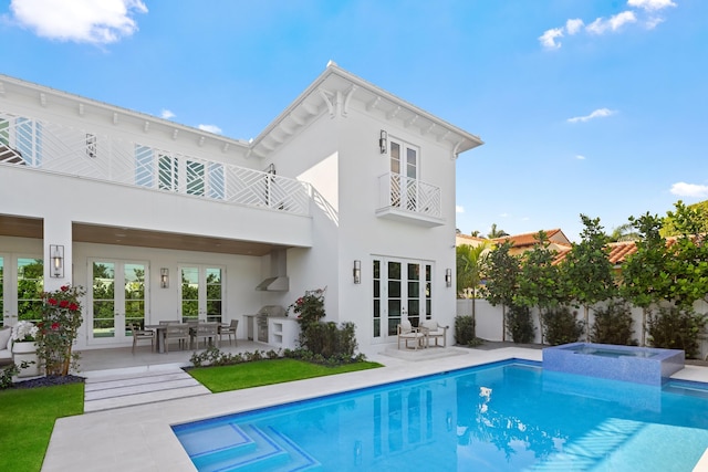 back of property featuring a balcony, a swimming pool with hot tub, and a patio