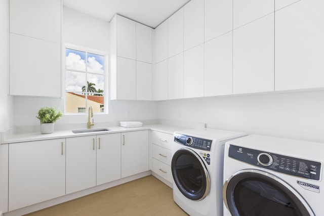 clothes washing area featuring cabinets, sink, washer and clothes dryer, and light hardwood / wood-style flooring