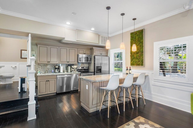 kitchen featuring dark wood-type flooring, appliances with stainless steel finishes, a kitchen bar, and a healthy amount of sunlight