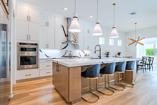 kitchen with a center island with sink, hanging light fixtures, sink, and white cabinetry