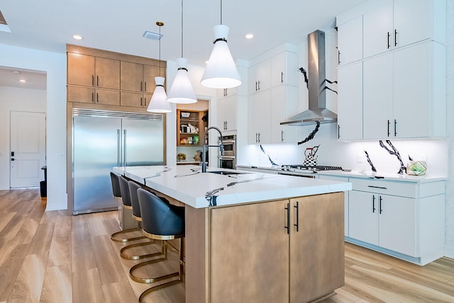 kitchen with an island with sink, decorative light fixtures, light hardwood / wood-style floors, and white cabinetry